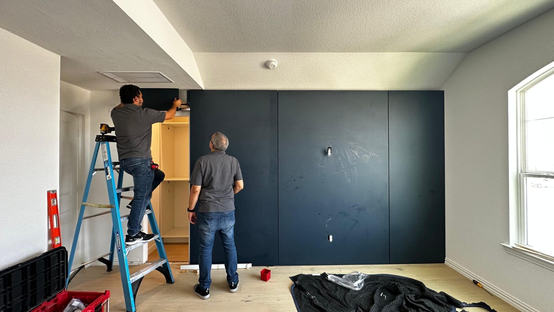 Two men are working on a wall in the room.